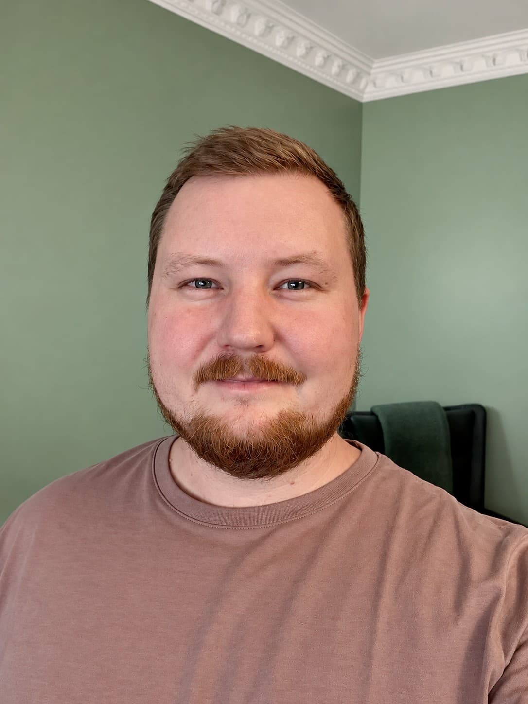 Hampus Malmström, smiling, with short red hair and a beard, in front of a green wall.
